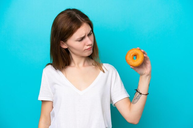 Jovem inglesa segurando um donut sobre fundo azul isolado com expressão triste