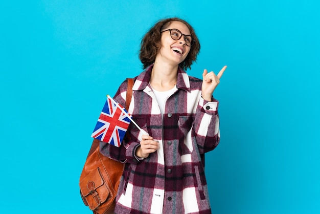 Jovem inglesa segurando uma bandeira do Reino Unido isolada em uma parede azul apontando uma ótima ideia