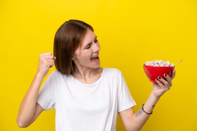 Jovem inglesa segurando uma xícara de café isolada em fundo amarelo comemorando uma vitória