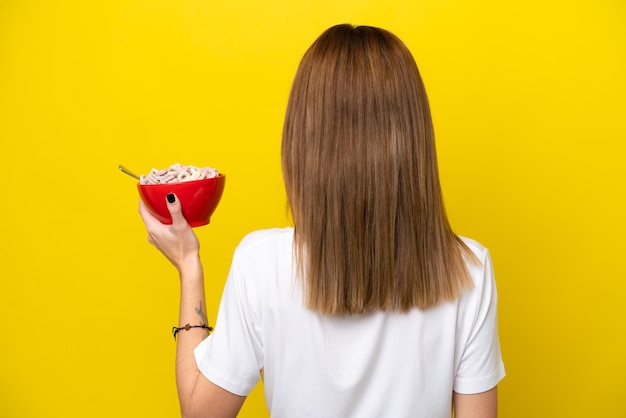 Jovem inglesa segurando uma xícara de café isolada em fundo amarelo na posição traseira