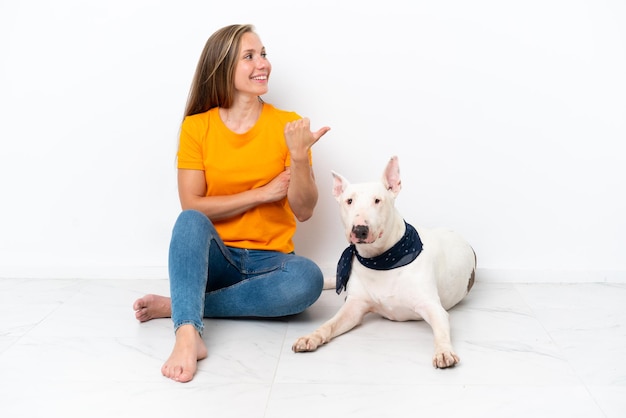 Jovem inglesa sentada no chão com seu cachorro isolado no fundo branco apontando para o lado para apresentar um produto