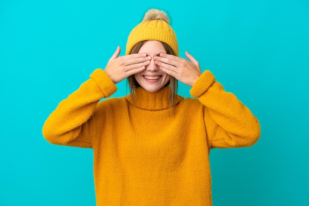 Jovem inglesa vestindo jaqueta de inverno isolada em fundo azul cobrindo os olhos pelas mãos