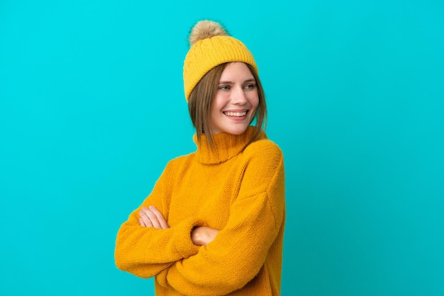 Jovem inglesa vestindo jaqueta de inverno isolada em fundo azul com braços cruzados e feliz