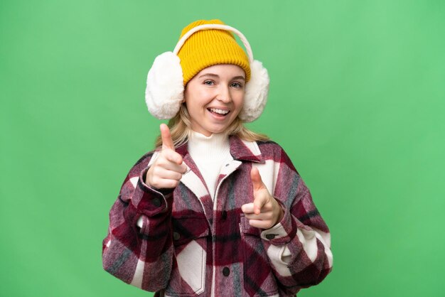 Jovem inglesa vestindo regalos de inverno sobre fundo isolado, apontando para a frente e sorrindo