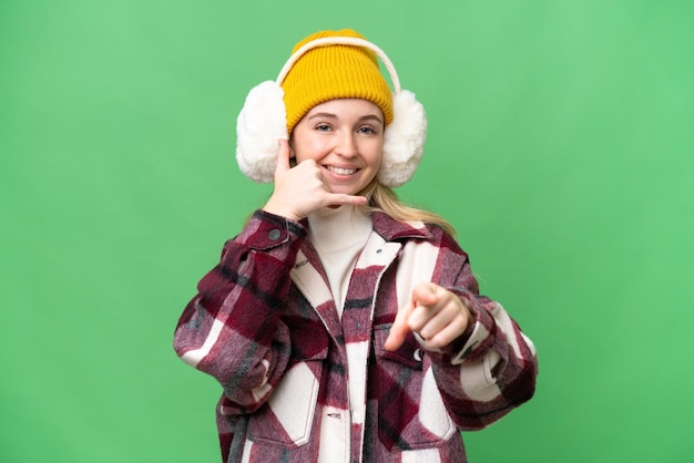 Jovem inglesa vestindo regalos de inverno sobre fundo isolado, fazendo gesto de telefone e apontando para a frente