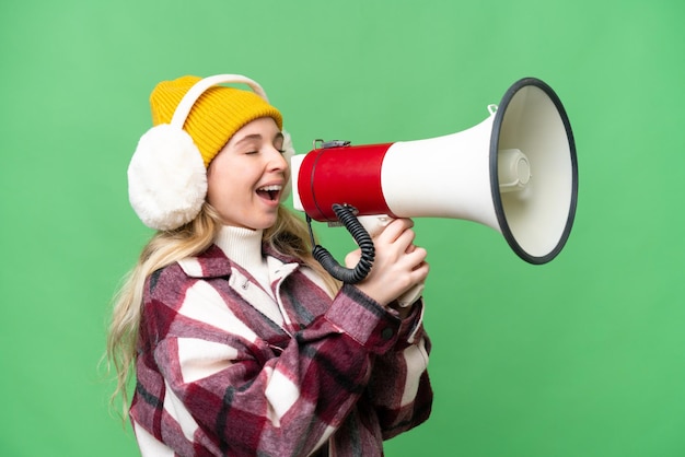 Jovem inglesa vestindo regalos de inverno sobre fundo isolado gritando através de um megafone