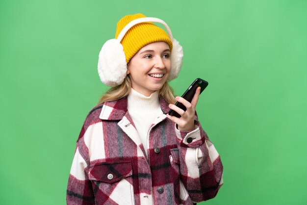 Jovem inglesa vestindo regalos de inverno sobre fundo isolado, mantendo uma conversa com o telefone celular