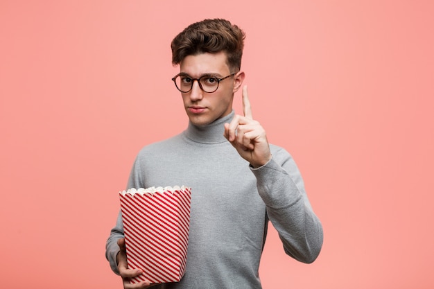 Jovem intelectual segurando um balde de pipoca, mostrando o número dois com os dedos.