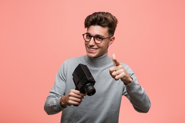 Jovem intelectual segurando um filme câmera alegre sorrisos apontando para a frente.