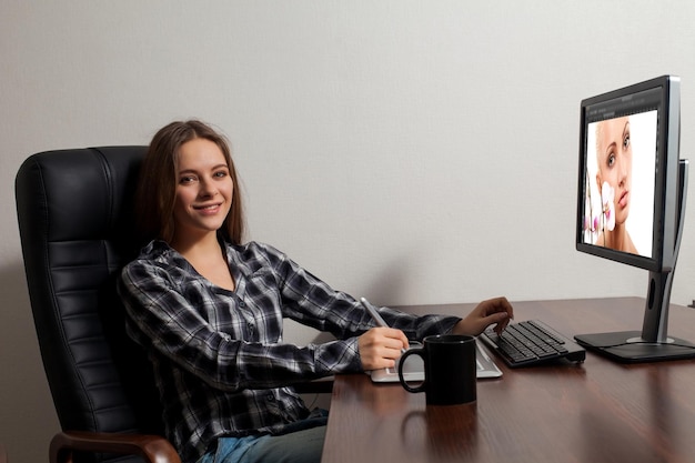 Jovem inteligente senta-se na frente do computador e faz seu trabalho de retoque durante o intervalo do café