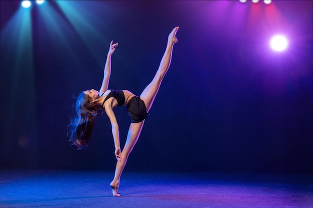 jovem intérprete de coreografia moderna dançando nos holofotes em um fundo preto