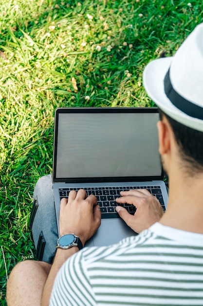 Jovem irreconhecível homem caucasiano usando um laptop sentado no gramado