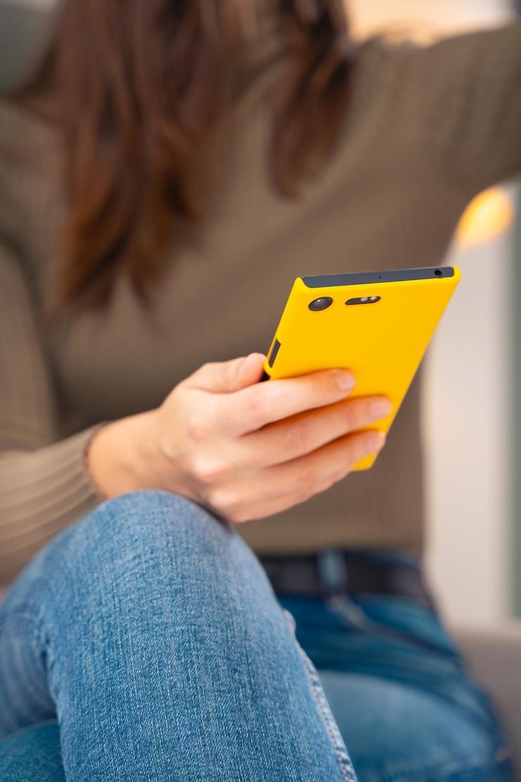 Foto jovem irreconhecível sentada em um sofá olhando para redes sociais com um smartphone vertical