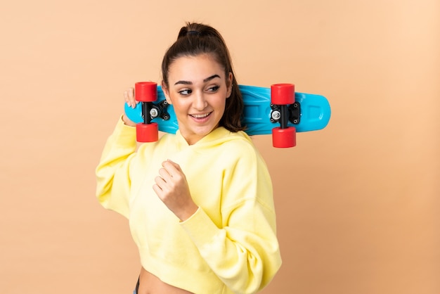 Jovem isolada na parede rosa com um skate com expressão feliz