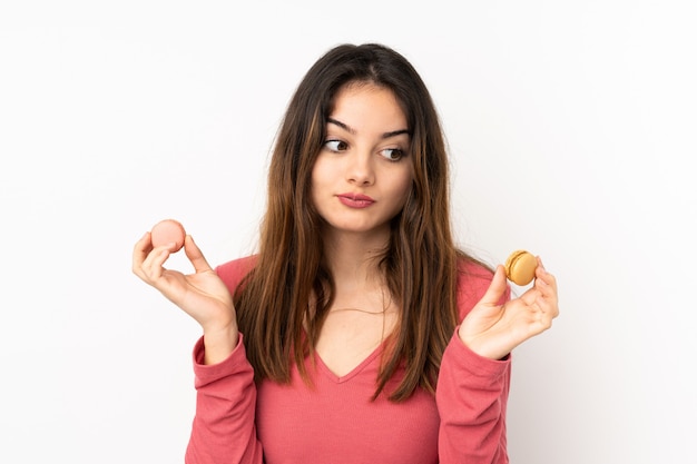 Jovem isolada na parede rosa segurando macarons franceses coloridos e infeliz