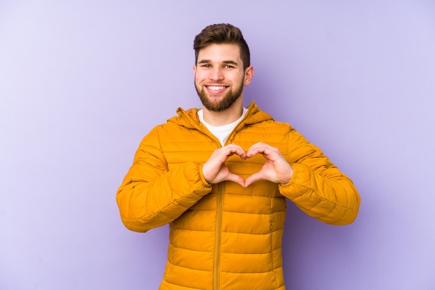 Jovem isolado em roxo sorrindo e mostrando uma forma de coração com as mãos.