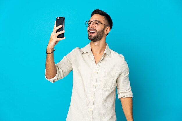 Jovem isolado na parede azul fazendo uma selfie