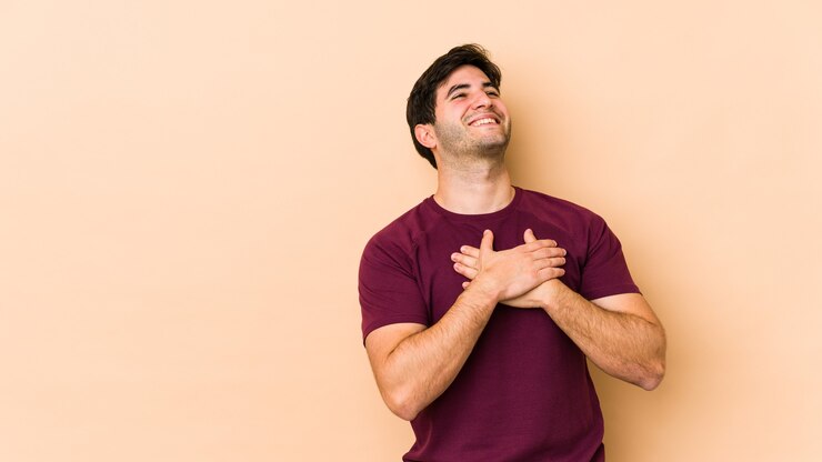 Foto jovem isolado no espaço bege rindo mantendo as mãos no coração, o conceito de felicidade.