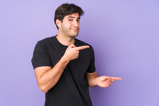 Jovem isolado no espaço roxo chocado apontando com o dedo indicador para um espaço de cópia.