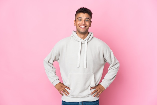 Jovem isolado posando com os braços na cintura e sorrindo