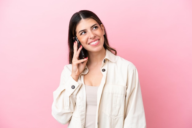 Jovem italiana isolada em fundo rosa, mantendo uma conversa com o celular com alguém