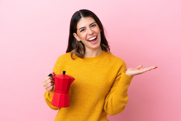 Jovem italiana segurando uma cafeteira isolada em fundo rosa com expressão facial chocada