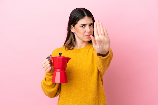 Foto jovem italiana segurando uma cafeteira isolada em fundo rosa fazendo gesto de parada