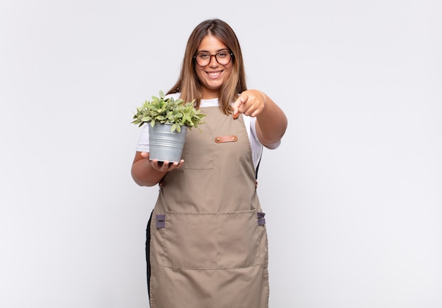 jovem jardineira apontando para a câmera com um sorriso satisfeito, confiante e amigável, escolhendo você