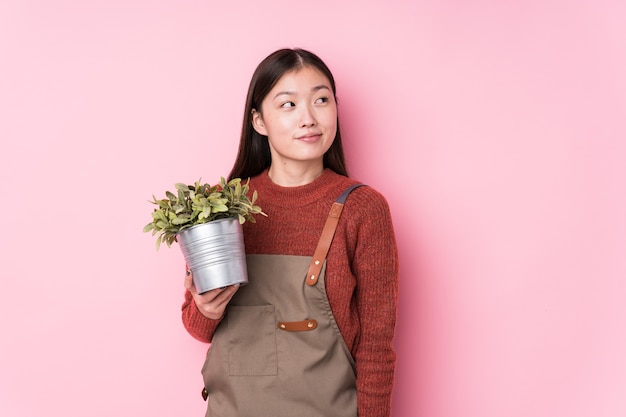 Jovem jardineira chinesa segurando uma planta isolada, sonhando em alcançar objetivos e propósitos