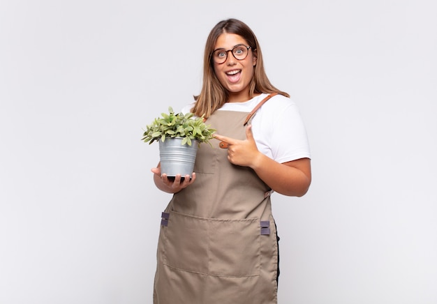 Jovem jardineira parecendo animada e surpresa, apontando para o lado e para cima para copiar o espaço