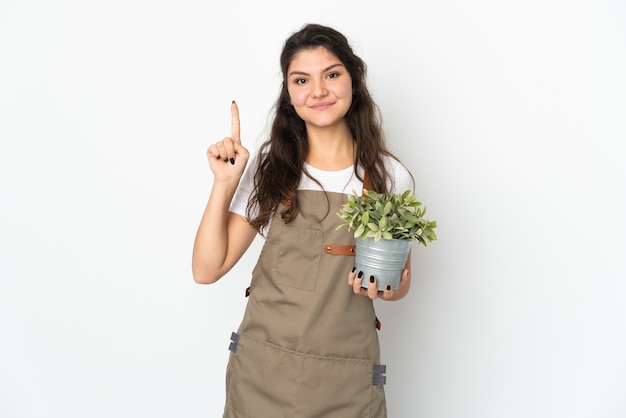 Jovem jardineira russa segurando uma planta isolada apontando para uma ótima ideia