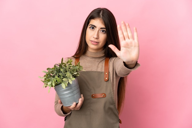 Jovem jardineira segurando uma planta isolada fazendo um gesto de parada