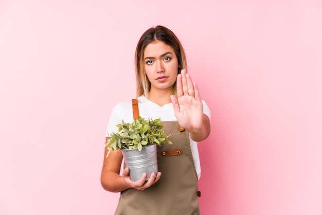 Jovem jardineiro caucasiana em uma superfície rosa de pé com a mão estendida, mostrando o sinal de pare, impedindo você.