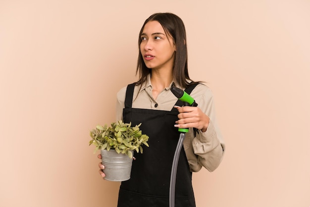 Jovem jardineiro colombiano segura uma planta e uma mangueira, cuidando da natureza.