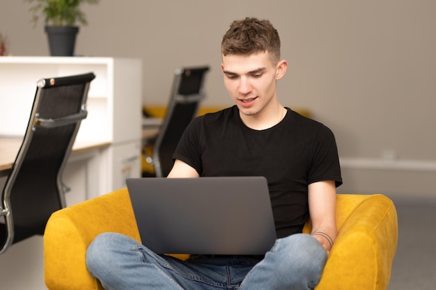 Jovem jogador bonito sentado no sofá e jogando no laptop