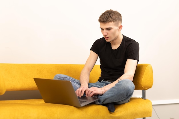 Jovem jogador bonito sentado no sofá e jogando no laptop