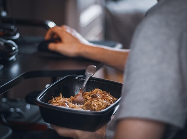 Jovem jogador caucasiano segurando um recipiente preto com comida wok durante a pausa do almoço