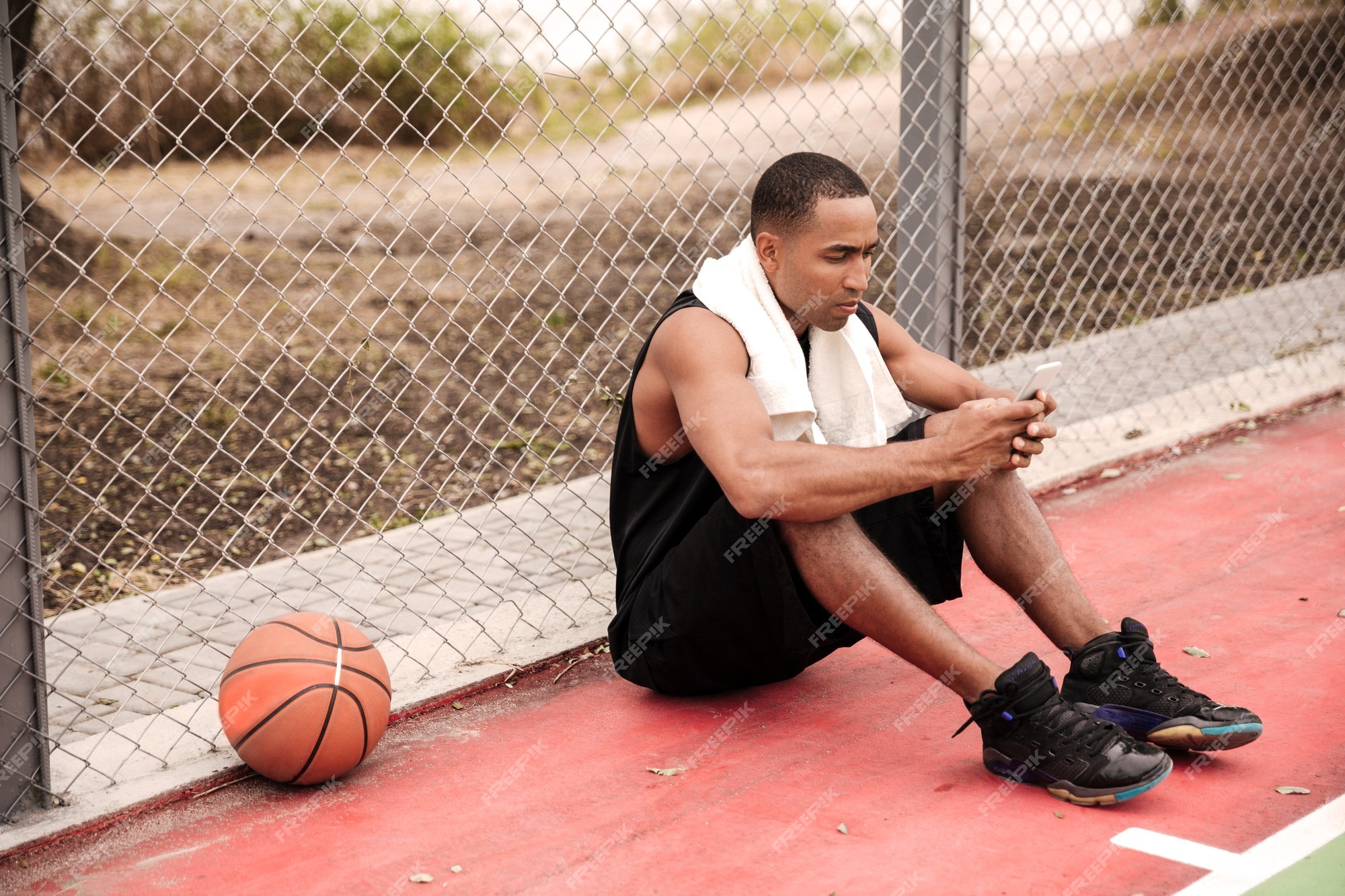 Jovem jogador de basquete feliz sentado no parque com uma toalha