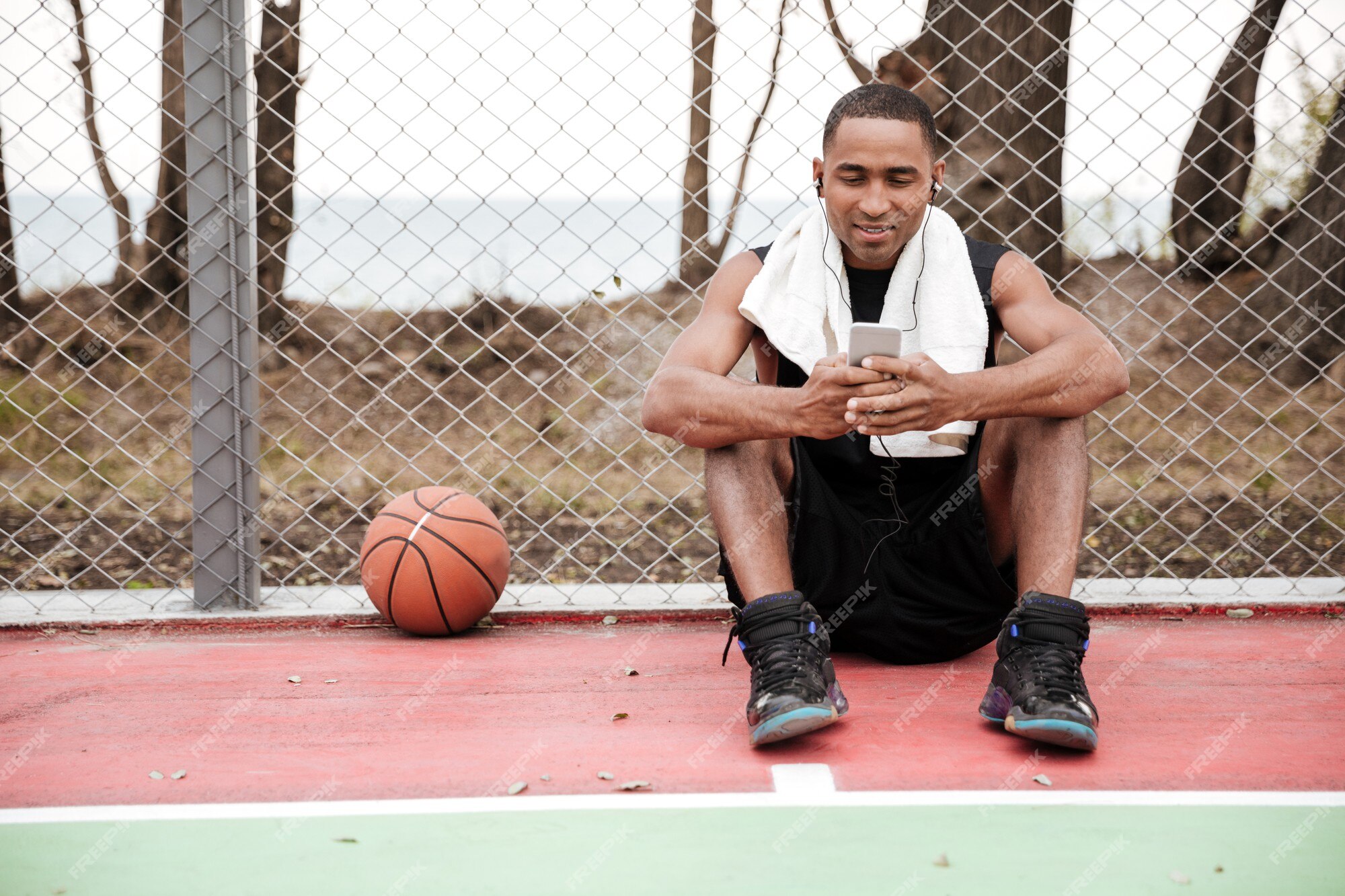 Jovem jogador de basquete feliz sentado no parque com uma toalha