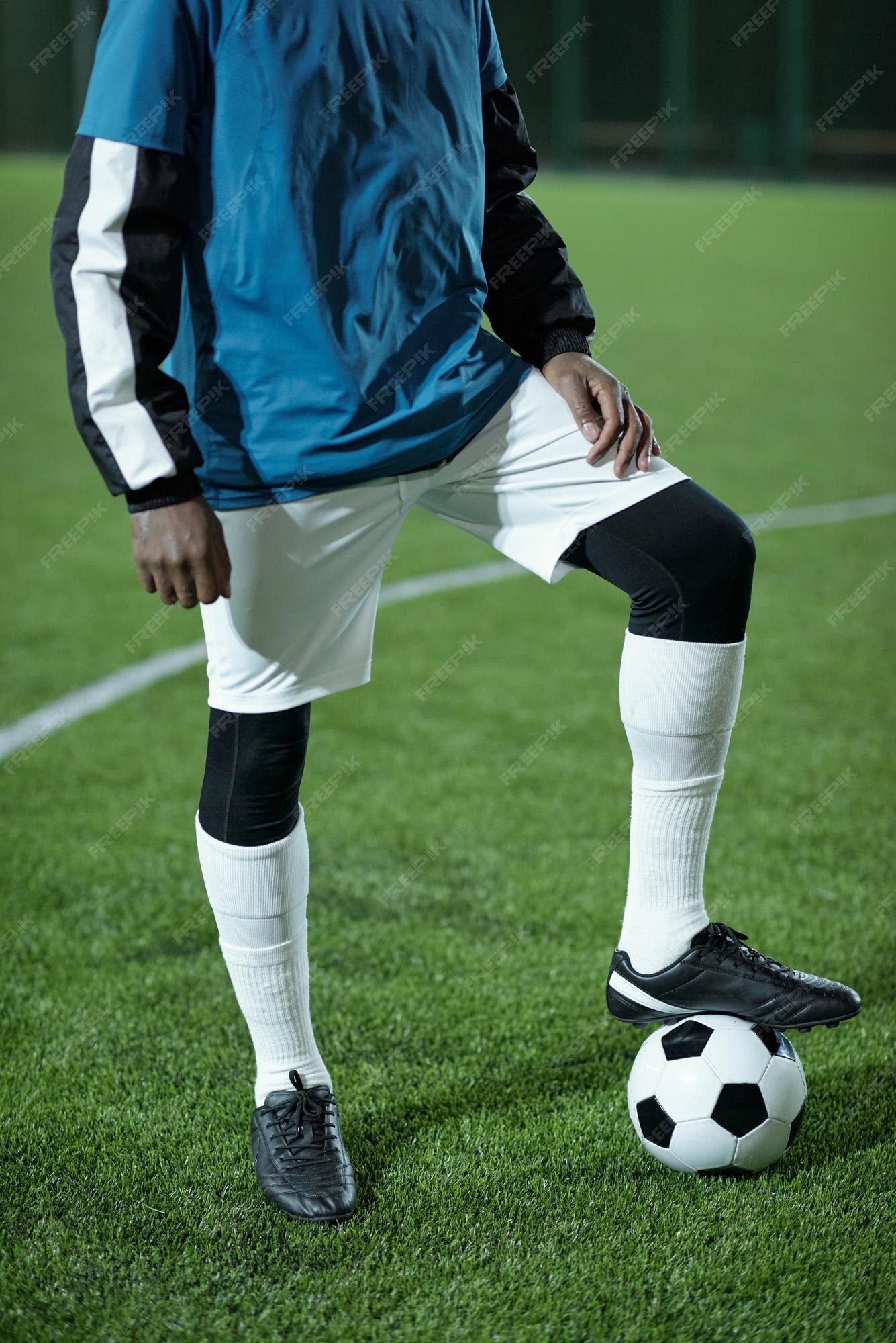 Jovem jogador de futebol africano uniformizado, mantendo os pés na