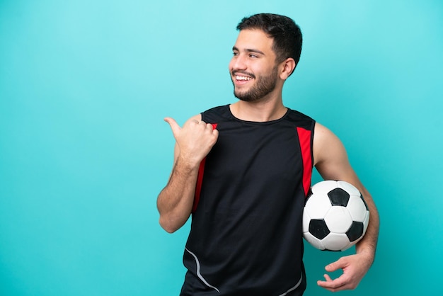 Jovem jogador de futebol brasileiro isolado em fundo azul apontando para o lado para apresentar um produto