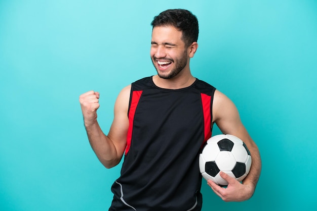 Jovem jogador de futebol brasileiro isolado em fundo azul comemorando uma vitória