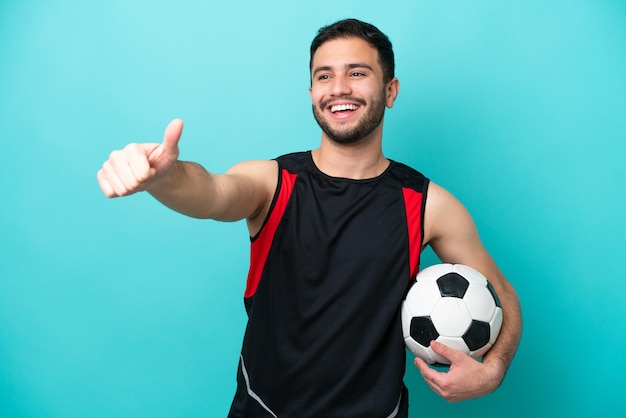 Jovem jogador de futebol brasileiro isolado em fundo azul dando um polegar para cima gesto