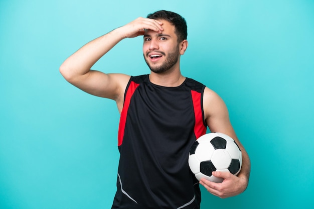 Jovem jogador de futebol brasileiro isolado em fundo azul fazendo gesto de surpresa enquanto olha para o lado