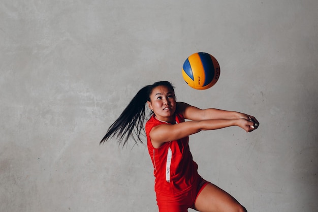 Jovem jogadora asiática de vôlei de uniforme vermelho pega bola