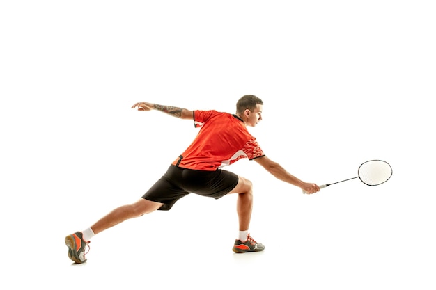 Jovem jogando badminton sobre fundo branco do estúdio. Atleta masculino apto isolado no branco. jogador de badminton em ação, movimento, movimento. conceito de ataque e defesa