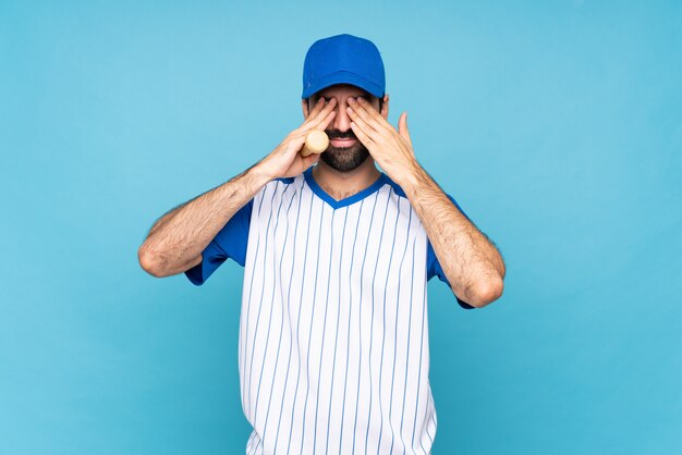 Jovem jogando beisebol isolado azul cobrindo os olhos pelas mãos