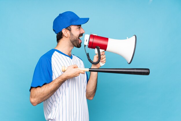 Jovem jogando beisebol isolado azul gritando através de um megafone