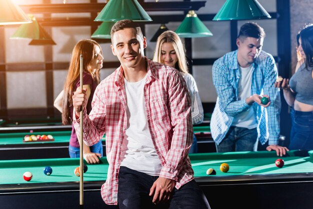 Jovem jogando bilhar. Posando perto da mesa com um taco nas mãos