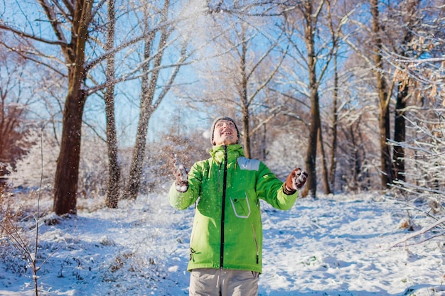 Jovem jogando neve na floresta de inverno se divertindo ao ar livre em atividades de inverno